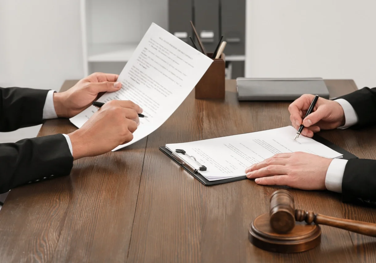 A person is holding papers and pen while another person holds a gavel.